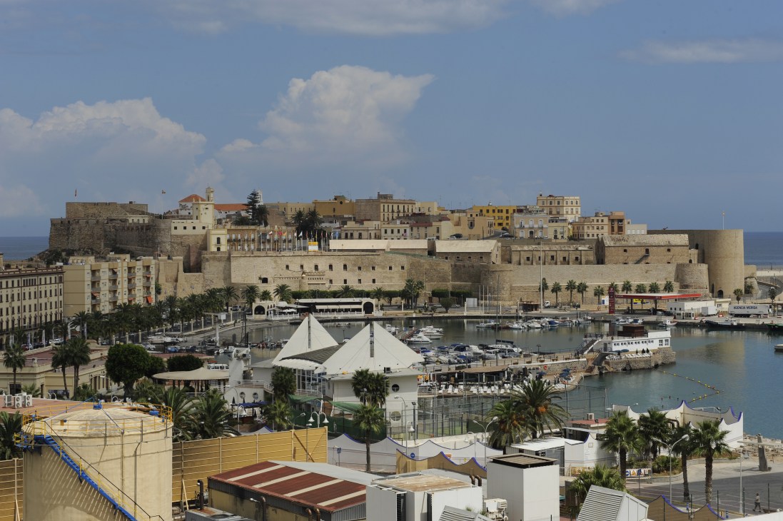 Melilla's port and old town with fortified walls, palm trees, and Mediterranean waterfront.