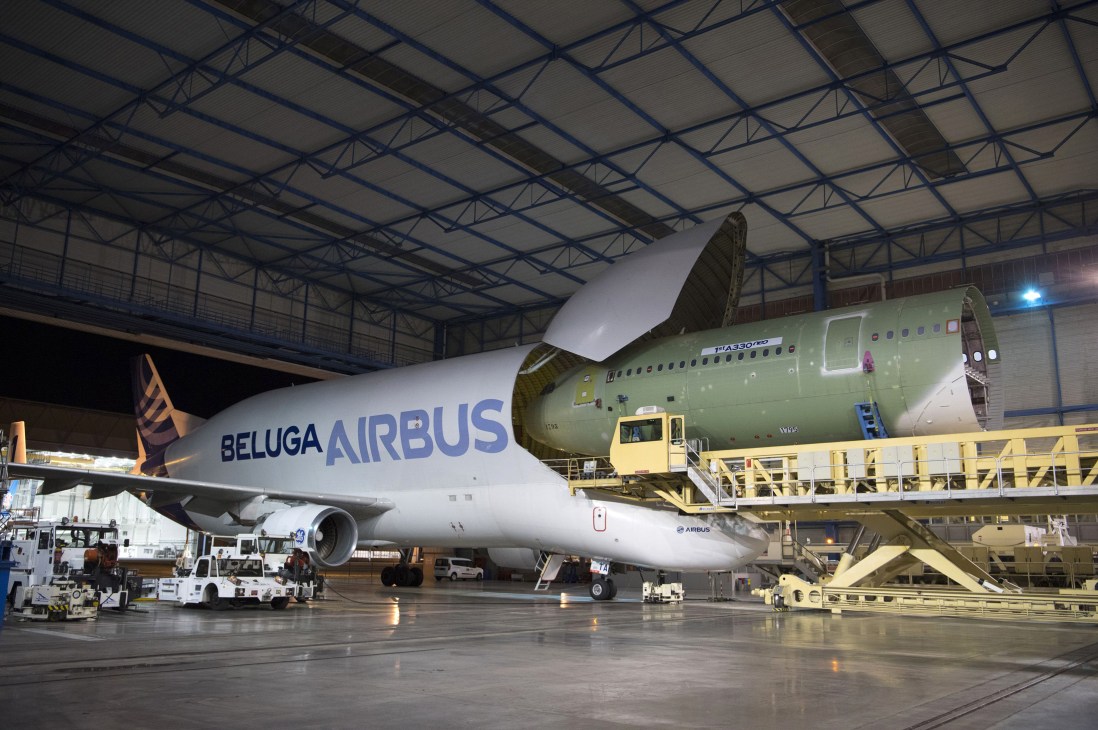 Large aircraft fuselage section being transported on ground equipment for assembly.