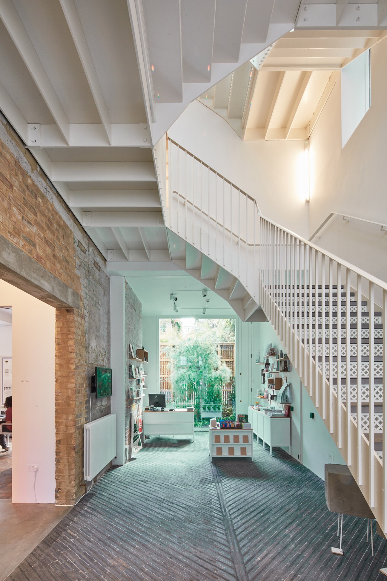Interior of South London Gallery annex showing exposed brick, white railings, wooden flooring and natural light from windows.