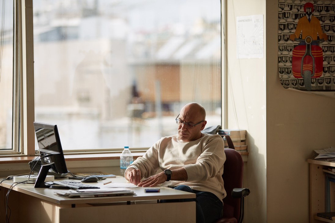 Man working at desk in modern office with large windows overlooking Athens cityscape.