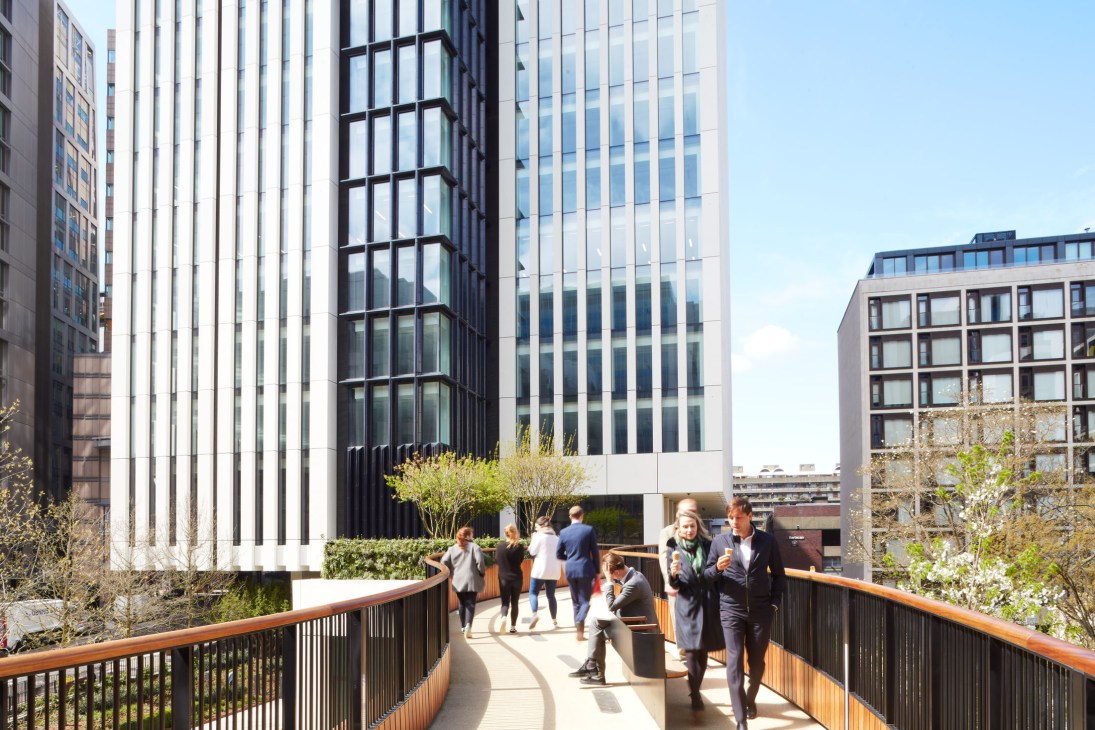 People walking on an elevated wooden-railed pathway between modern glass and steel buildings in London.