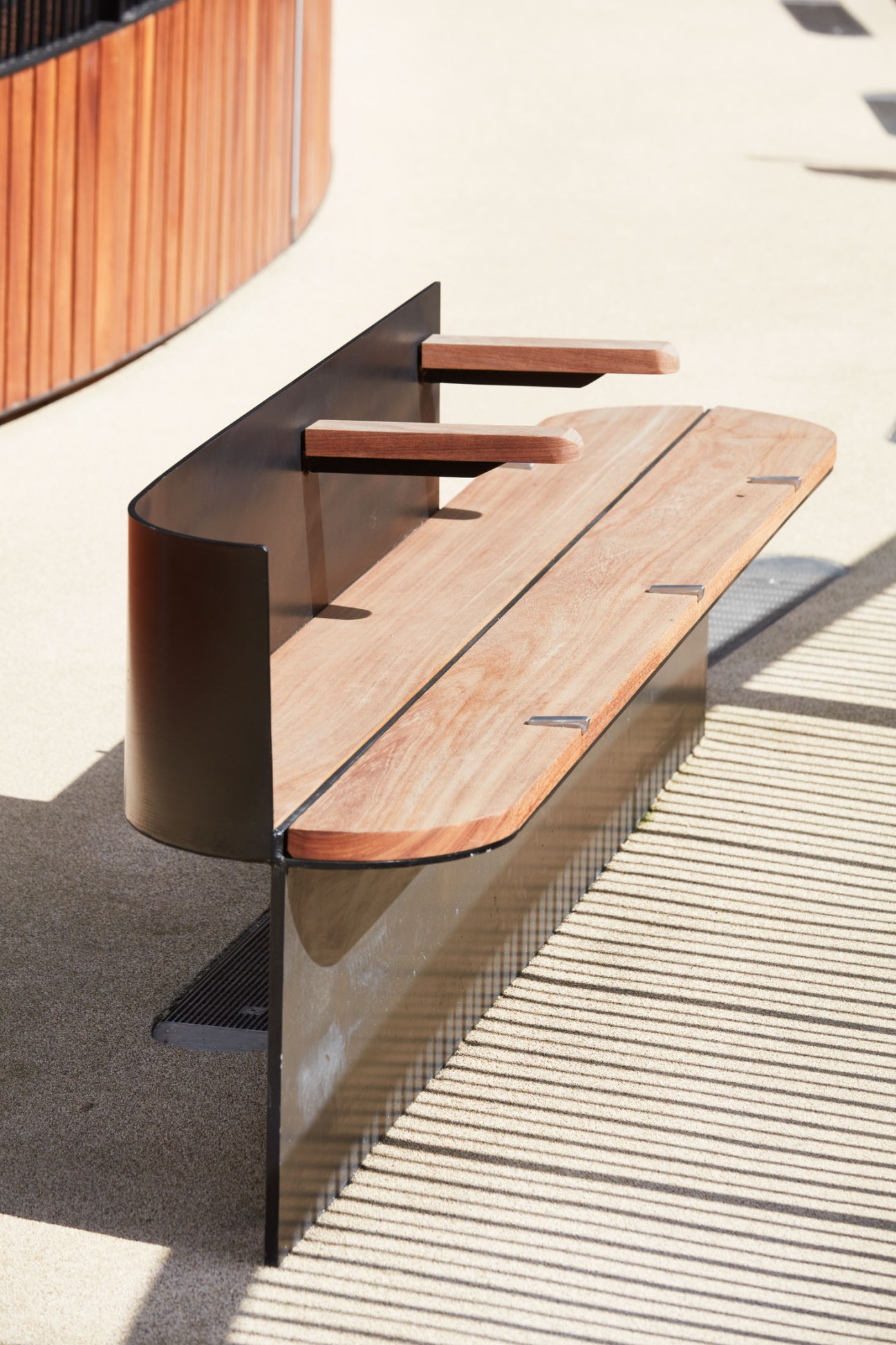 Wooden bench with backrest mounted on weathered steel structure at London Wall Place elevated walkway.
