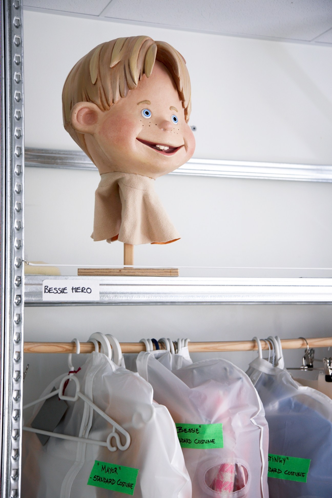 Puppet head of Ziggy character displayed above LazyTown costumes on a shelf.