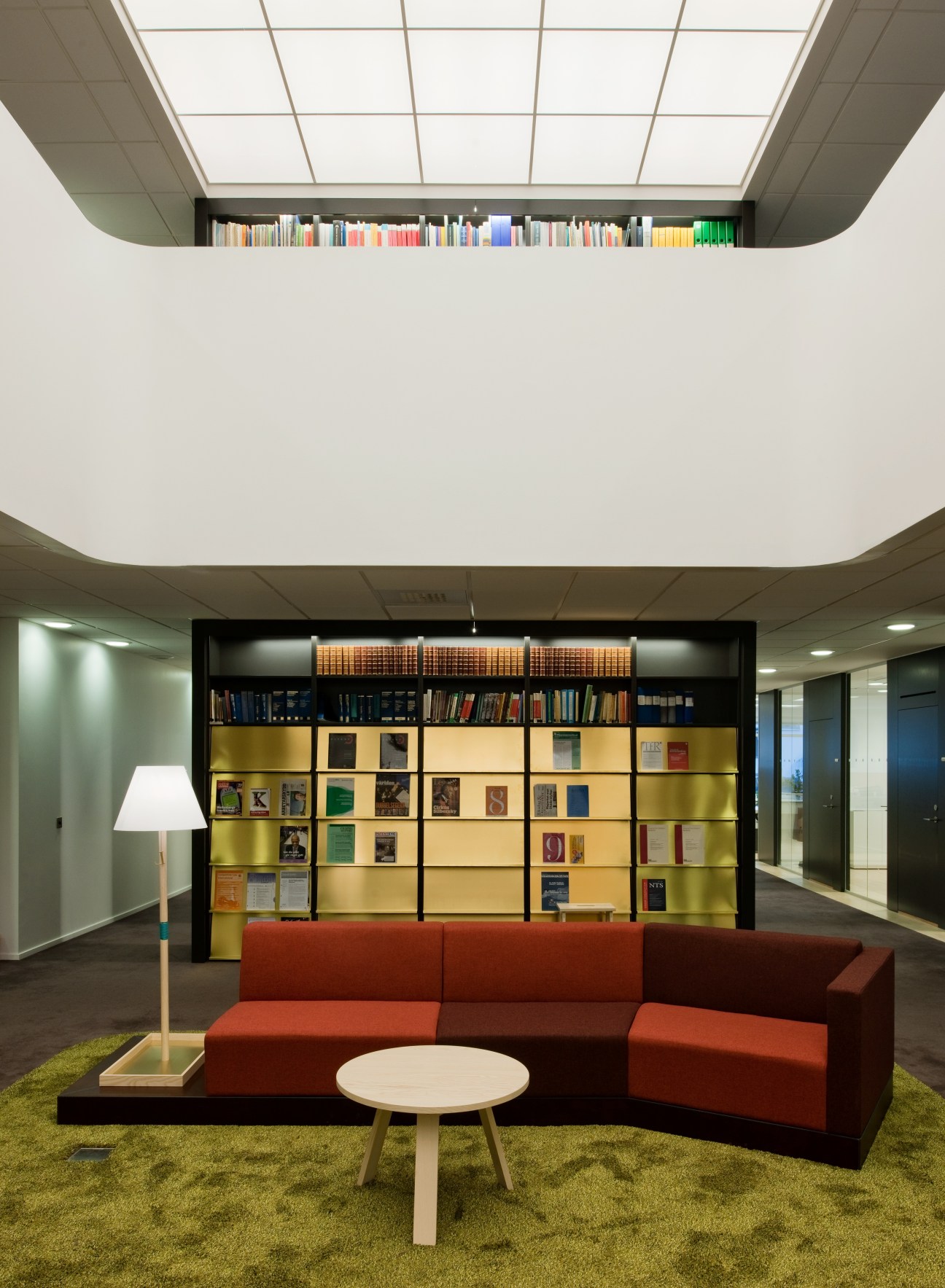 Library with back-lit glass ceiling, red sofa, gold-accented shelving, and colorful books.
