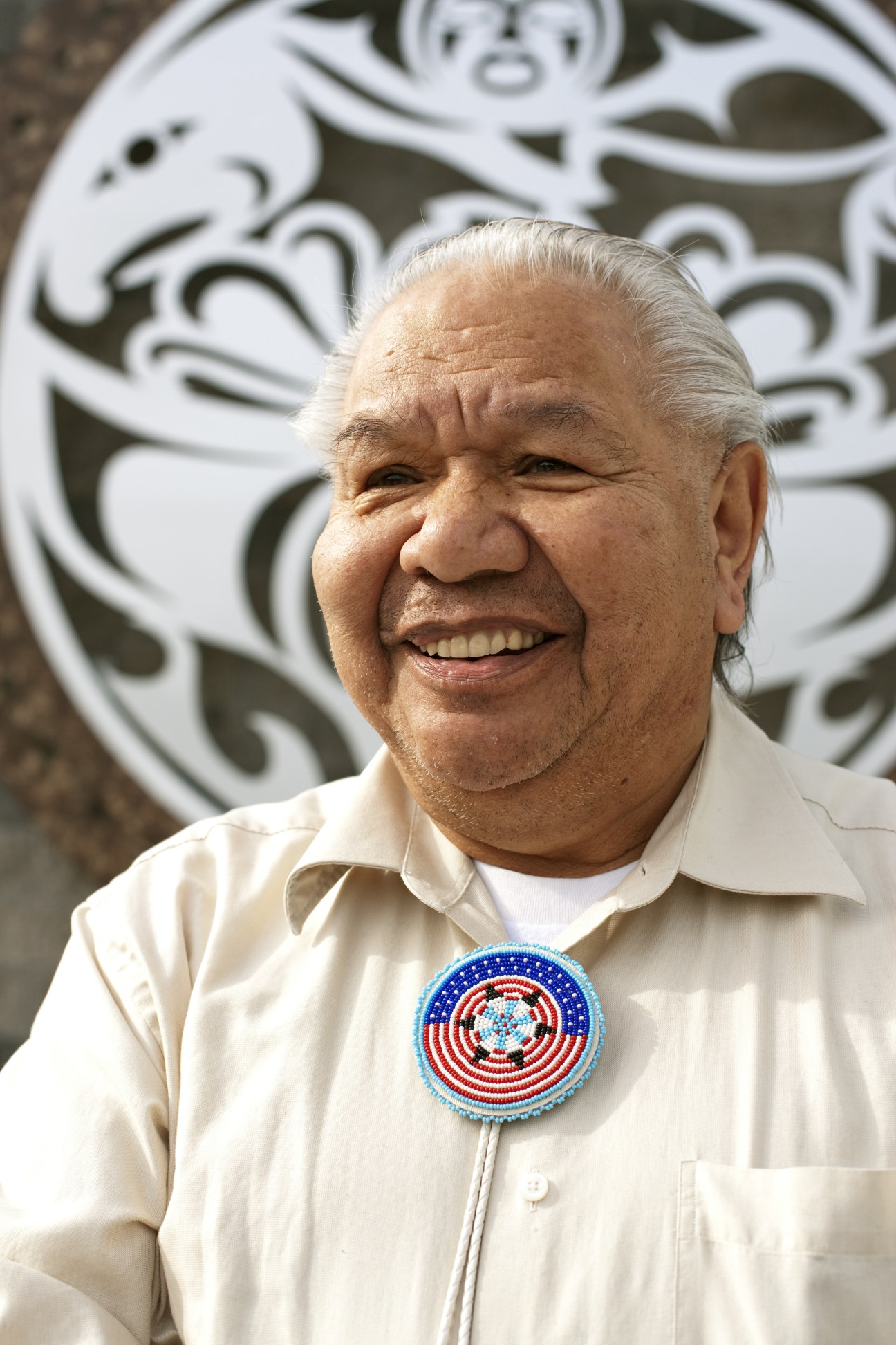 David Fryberg, a weaver of ceremonial hats, smiles at the camera wearing a beaded brooch.