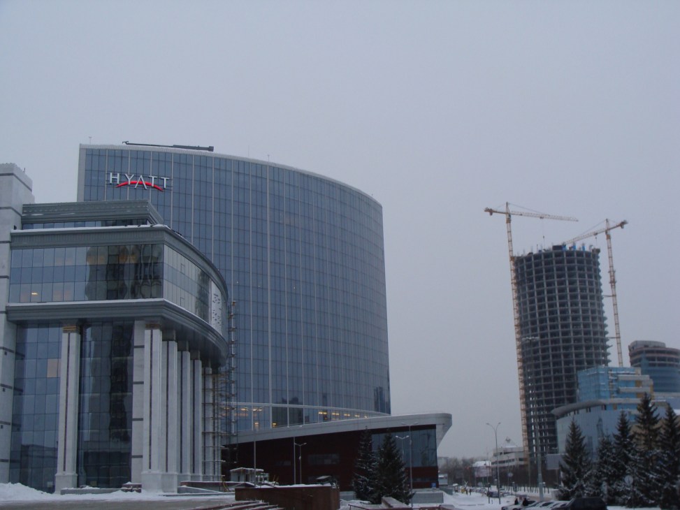 Newly built Hyatt hotel with glass facade next to construction cranes in snowy Ekaterinburg.