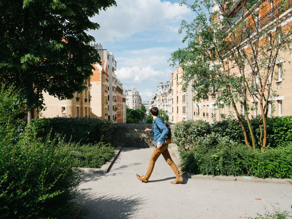 A man in a blue jacket jogs along a tree-lined Paris street with planted pots on either side.
