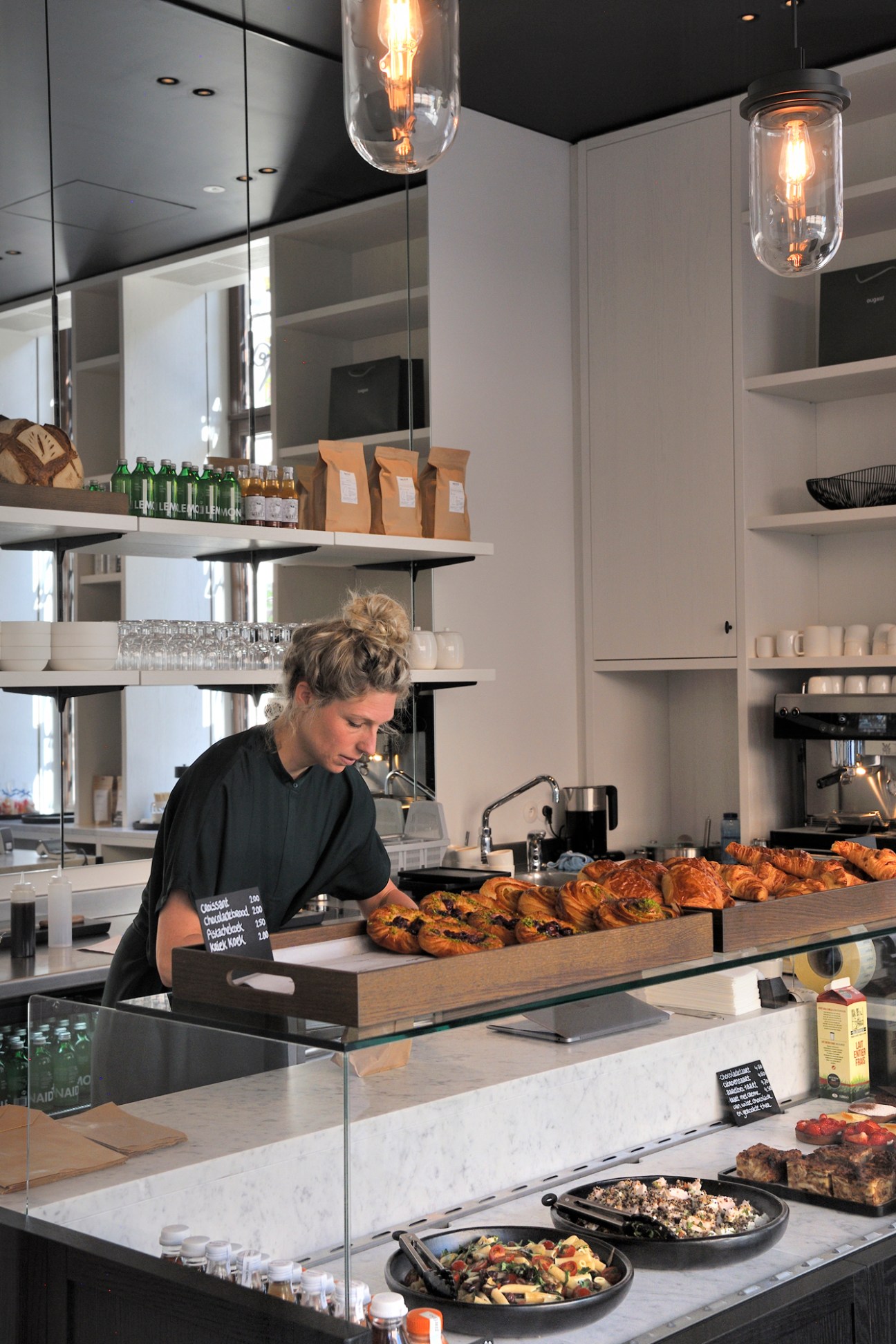 Staff member at Domestic bakery counter with fresh pastries and baked goods displayed.
