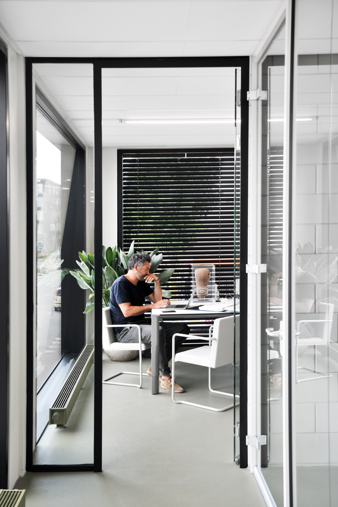 Creative director Emile Kuenen sitting at a white desk in a modern glass-walled office with horizontal blinds