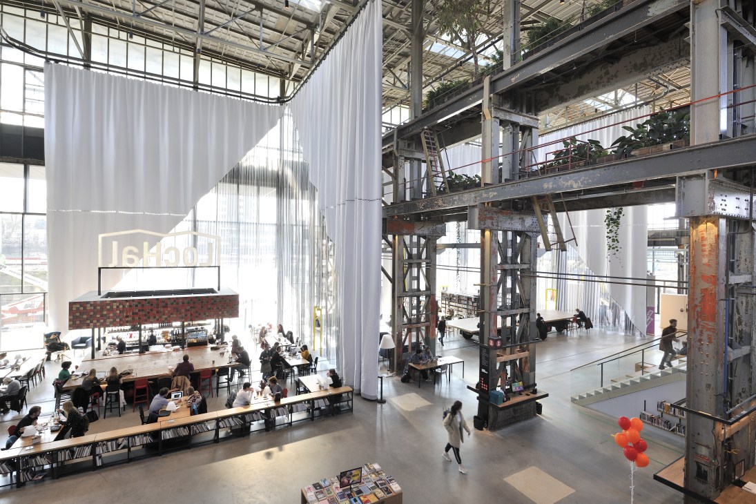 Interior view of LocHal library with industrial steel structure, hanging textile dividers, and people using the public space.