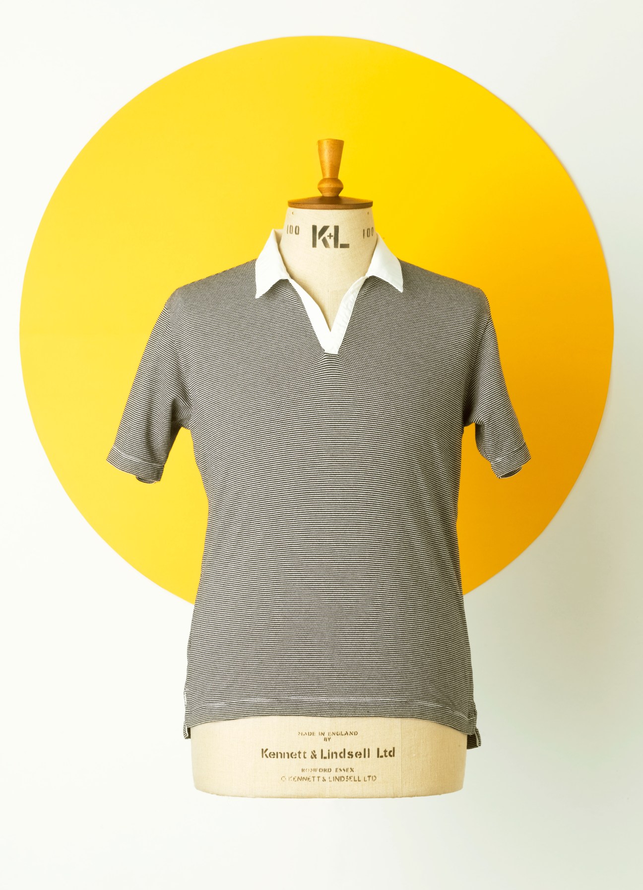 Grey striped polo shirt on a dress form with white collar against a yellow circular backdrop.