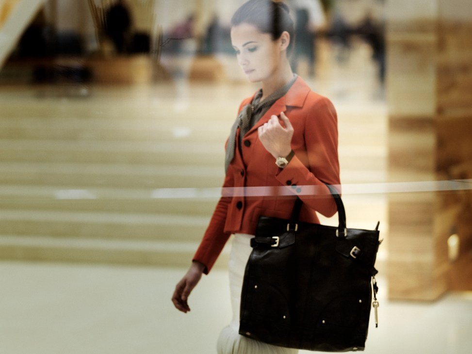Woman wearing red Gucci jacket and silk blouse with black Hugo Boss leather bag and TAG Heuer watch in modern office setting.