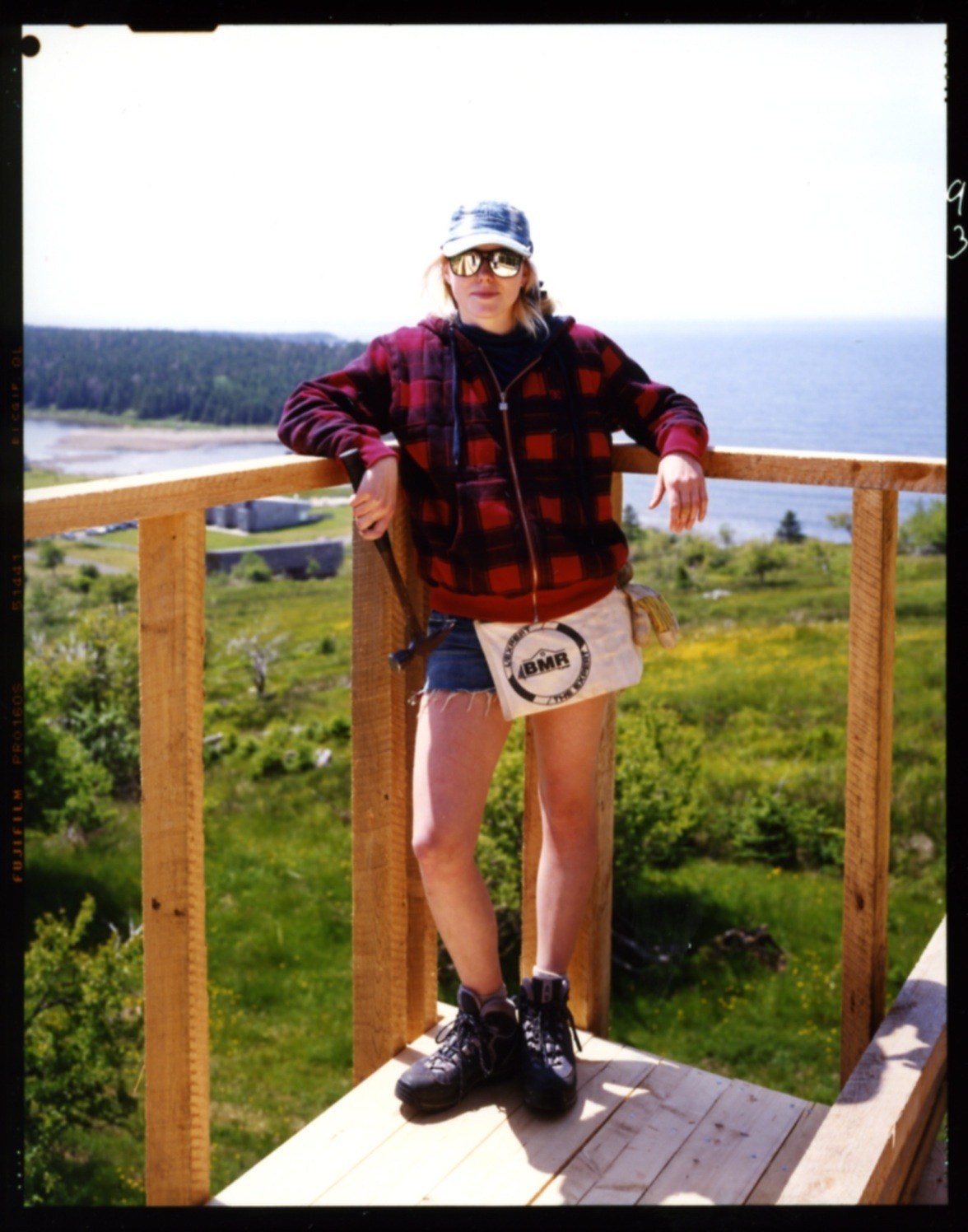 Student Maegan Magathan stands on a wooden deck railing overlooking a forested Nova Scotia landscape with water visible in the distance.