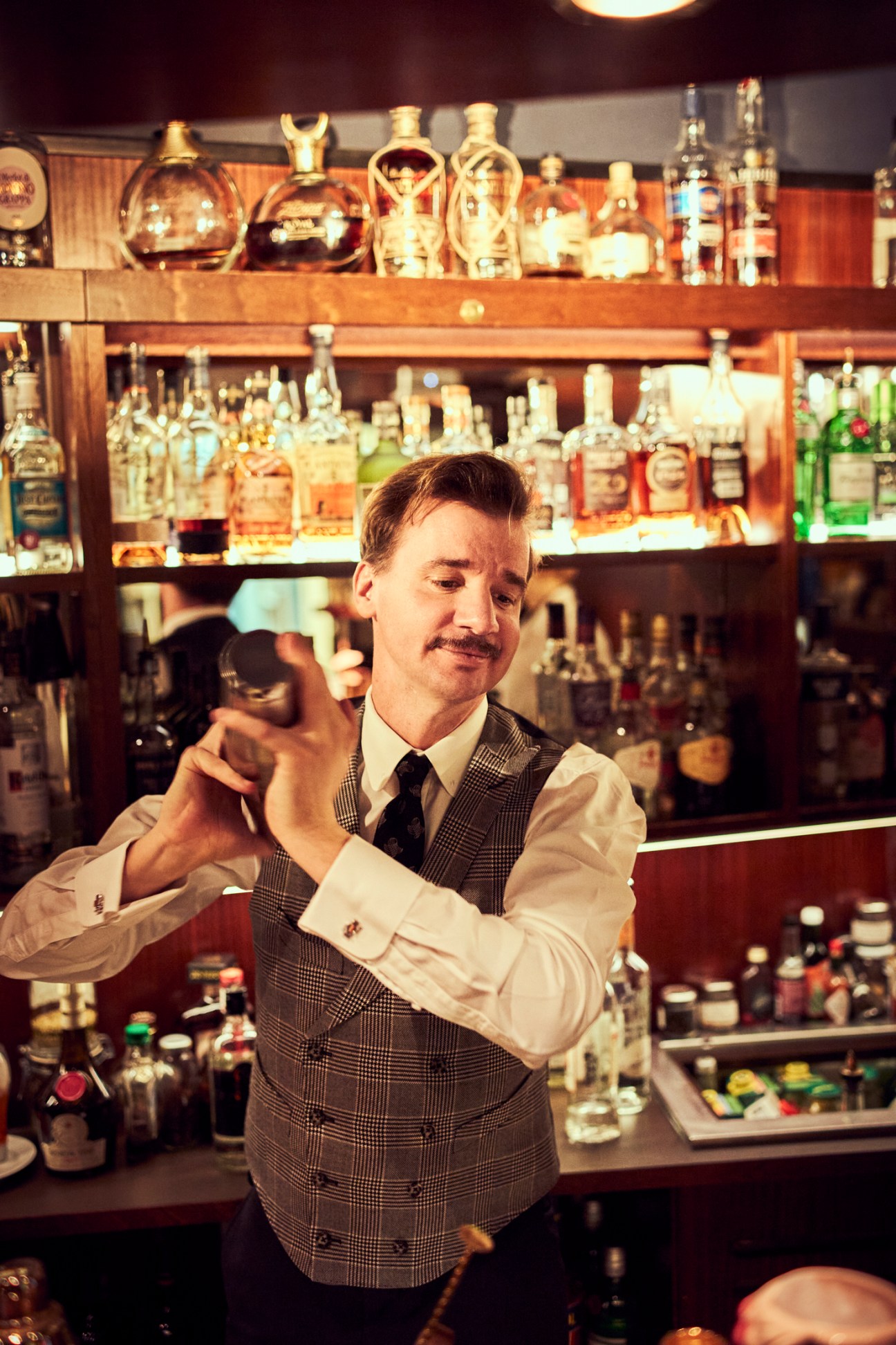 Bartender in vest and tie making cocktails behind bar with extensive bottle collection at Ernst Fuchs Bar