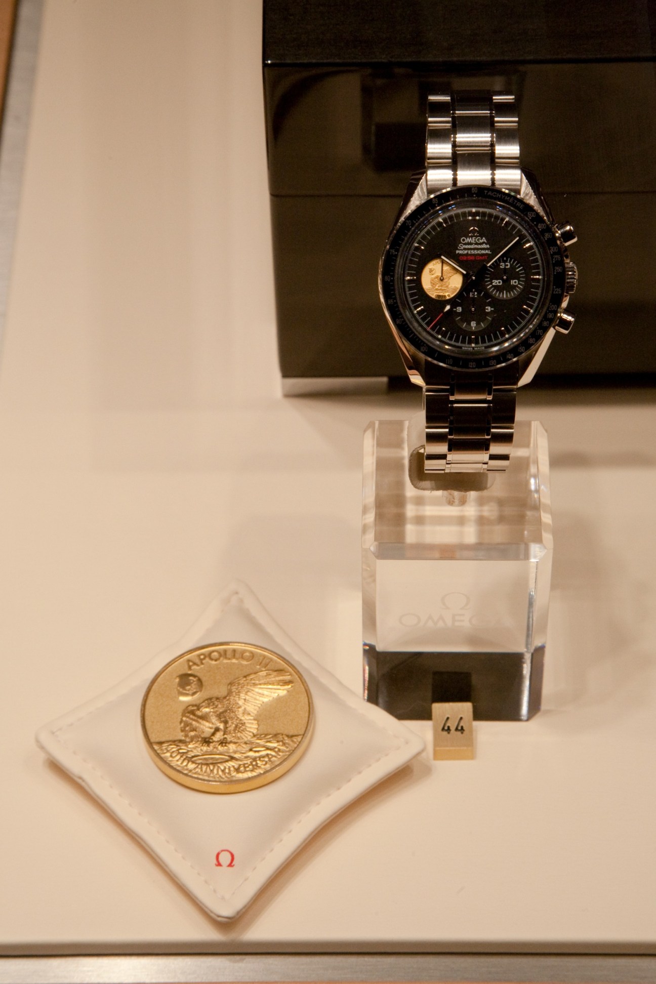 Omega Speedmaster Professional chronograph watch displayed on stand with Apollo 11 commemorative coin.