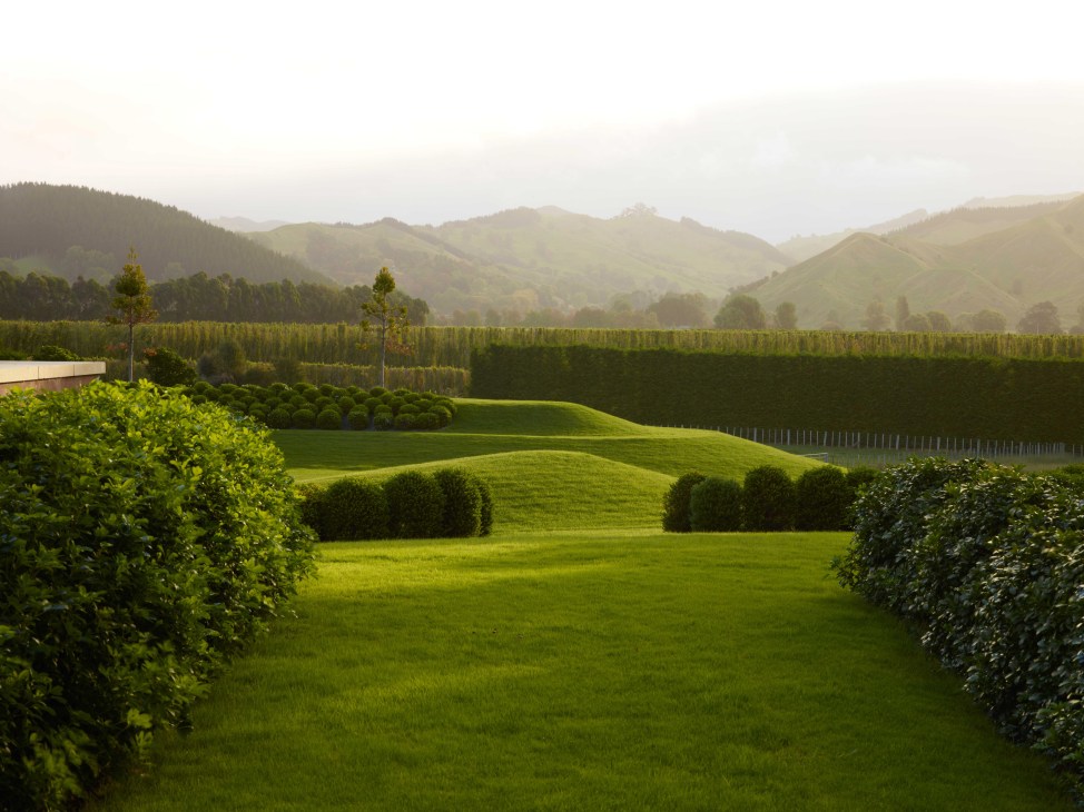 Rolling green landscape with manicured hedges and distant forested mountains at Orongo Station.