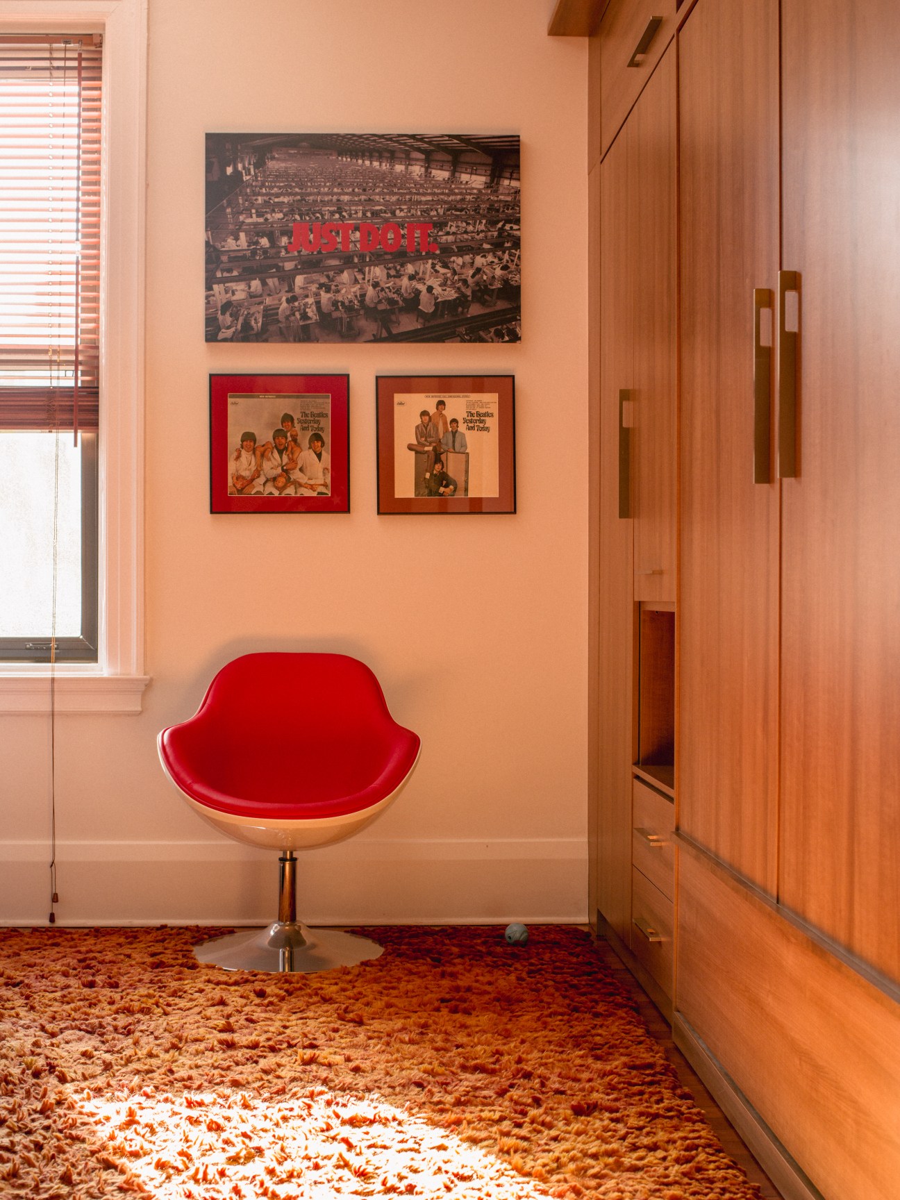 Red mid-century modern chair with wooden base against peach wall displaying framed Beatles album covers and vintage photographs.