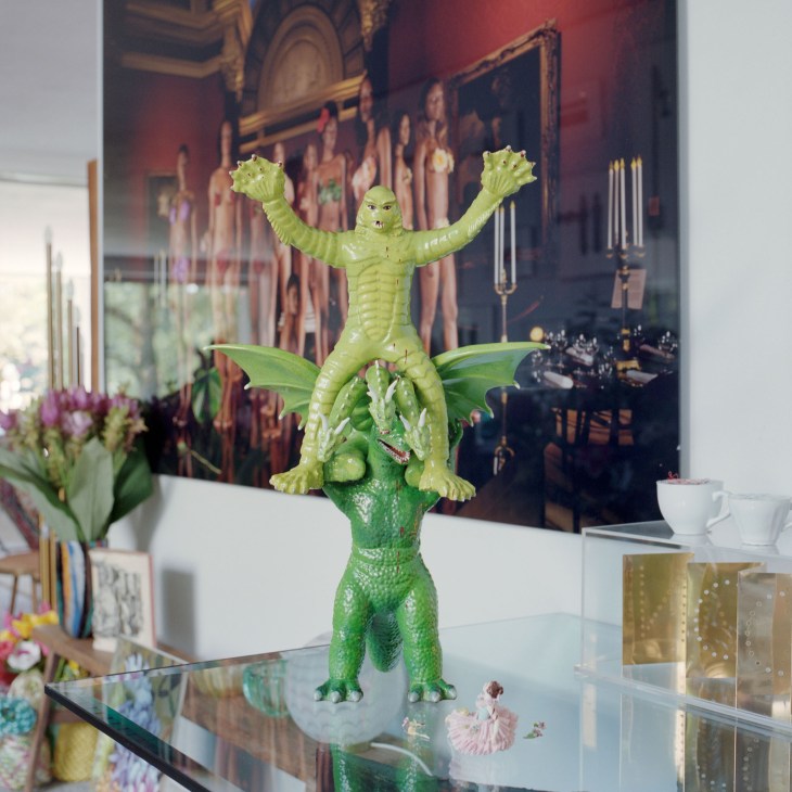 A vintage green plastic creature toy with raised arms displayed on a glass table among eclectic home decor.