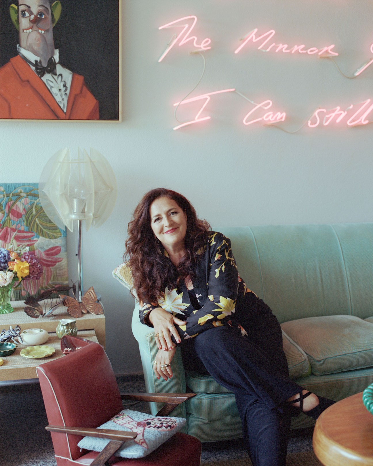 Angela Missoni sits on a green corduroy couch in her modernist living room decorated with eclectic artworks and vintage furnishings.
