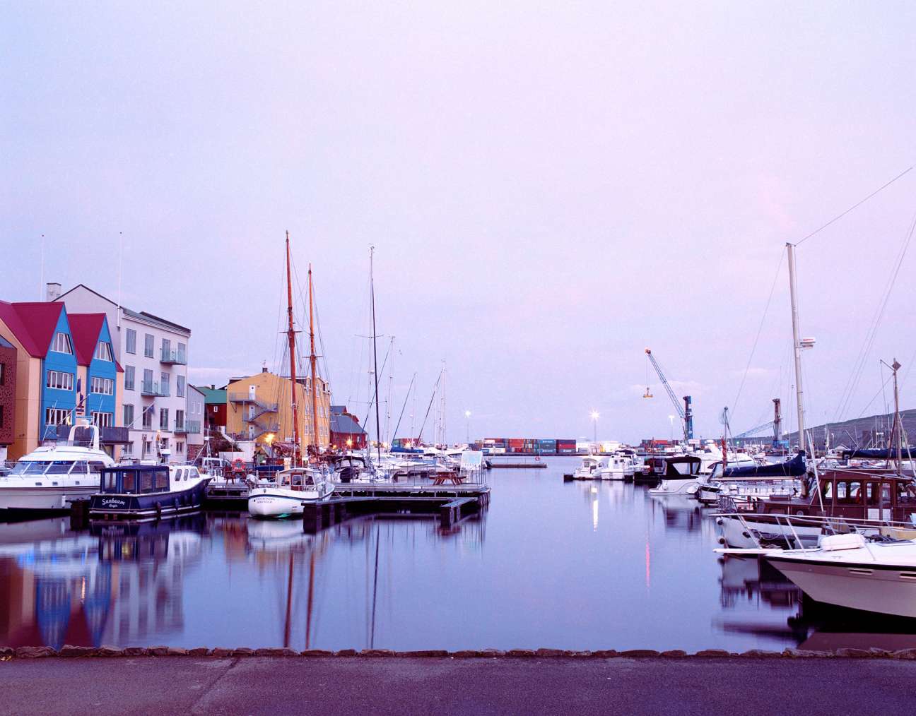 Tórshavn harbour at dusk with colourful buildings, sailboats, and calm water under purple sky.