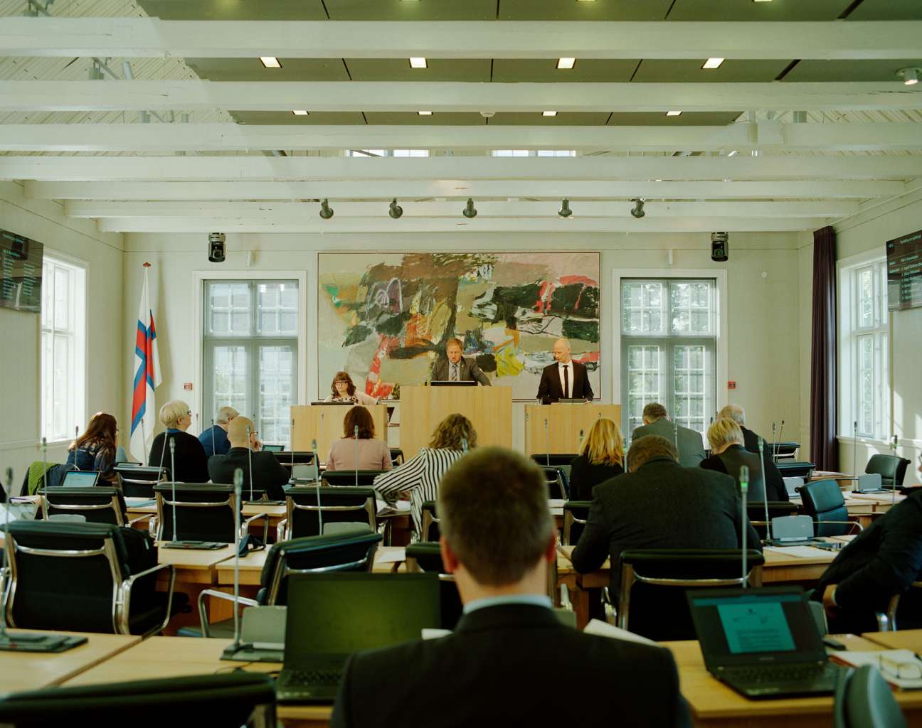 Interior of the Løgting parliament chamber with legislators seated at desks facing a raised speaker's platform.
