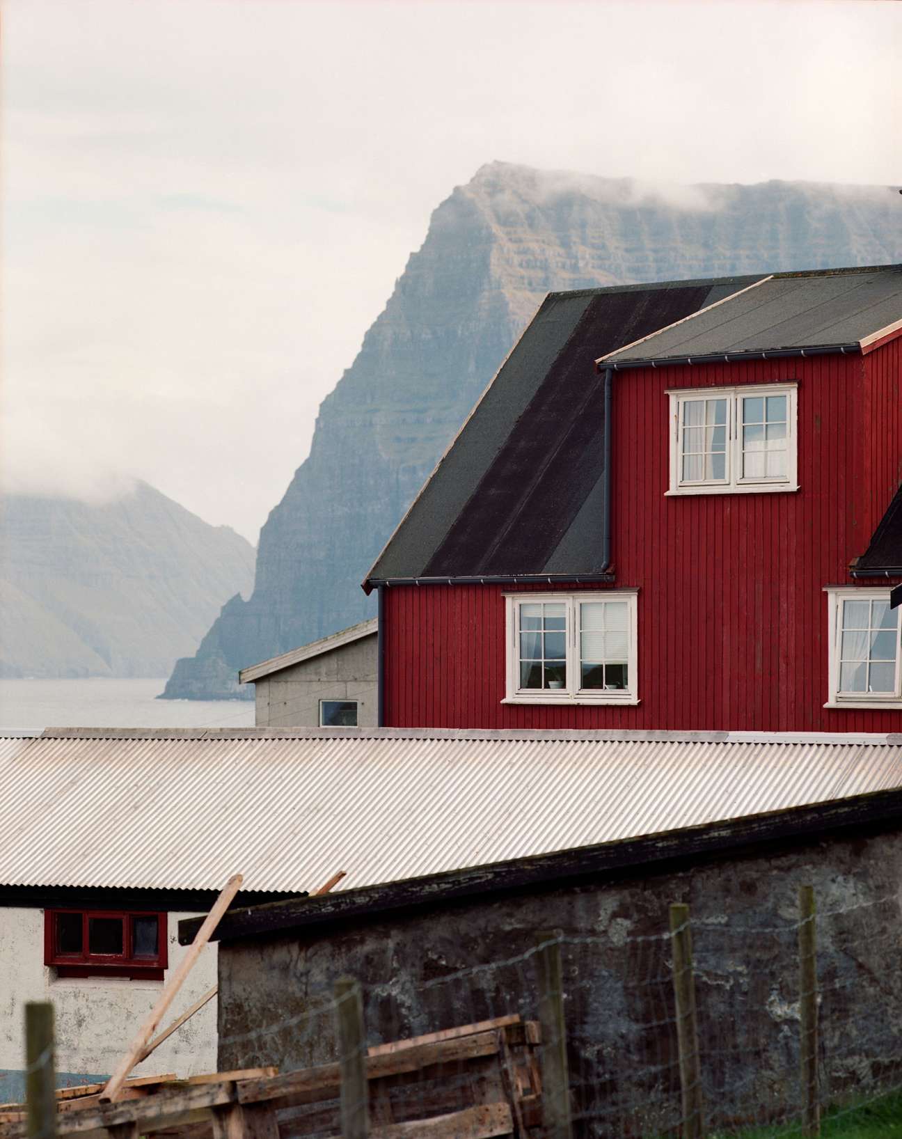 Red wooden house with white windows on Kalsoy island, backed by dramatic rocky cliffs.