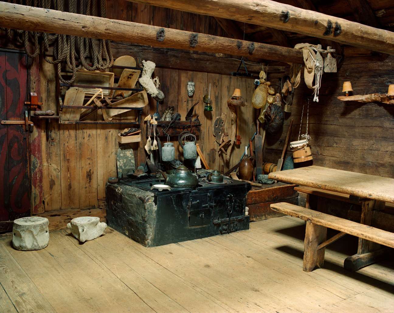 Interior of a historic Faroese farmhouse with wooden beams, traditional furnishings, and farming implements on display.