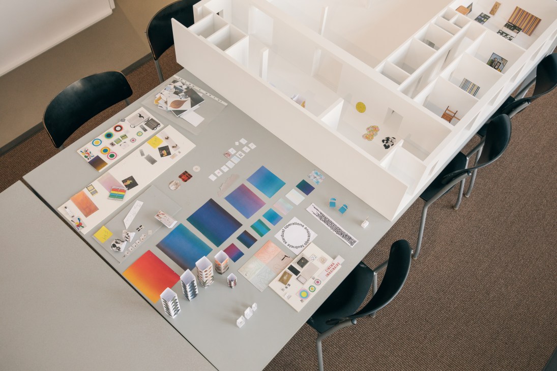 Gallery exhibition plan with color swatches, sketches and architectural samples organized on a table.
