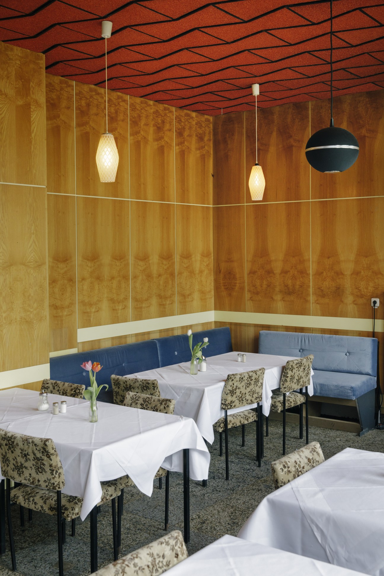 Milchbar restaurant dining room with set tables, wood-paneled walls, and pendant lighting