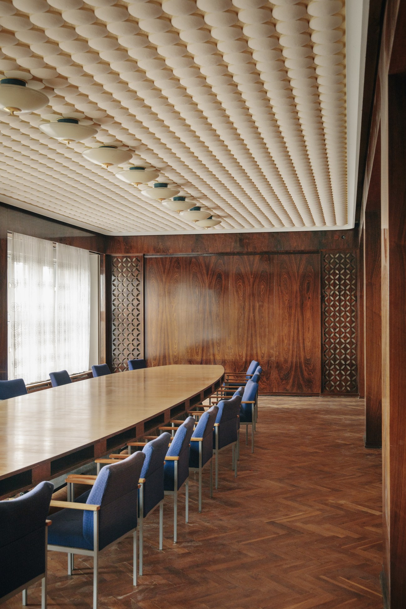 Historic GDR Broadcasting Committee meeting room with wood paneling, long table, and geometric ceiling design.