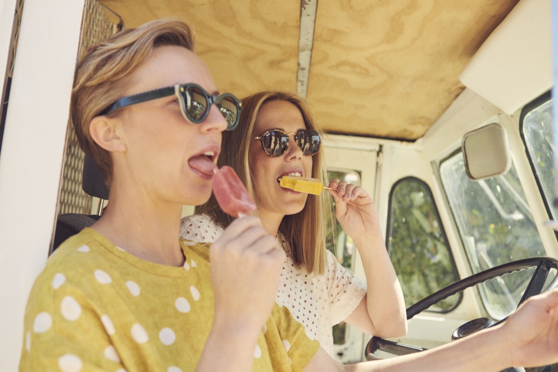 Two women eating ice cream and popsicles inside a yellow van.
