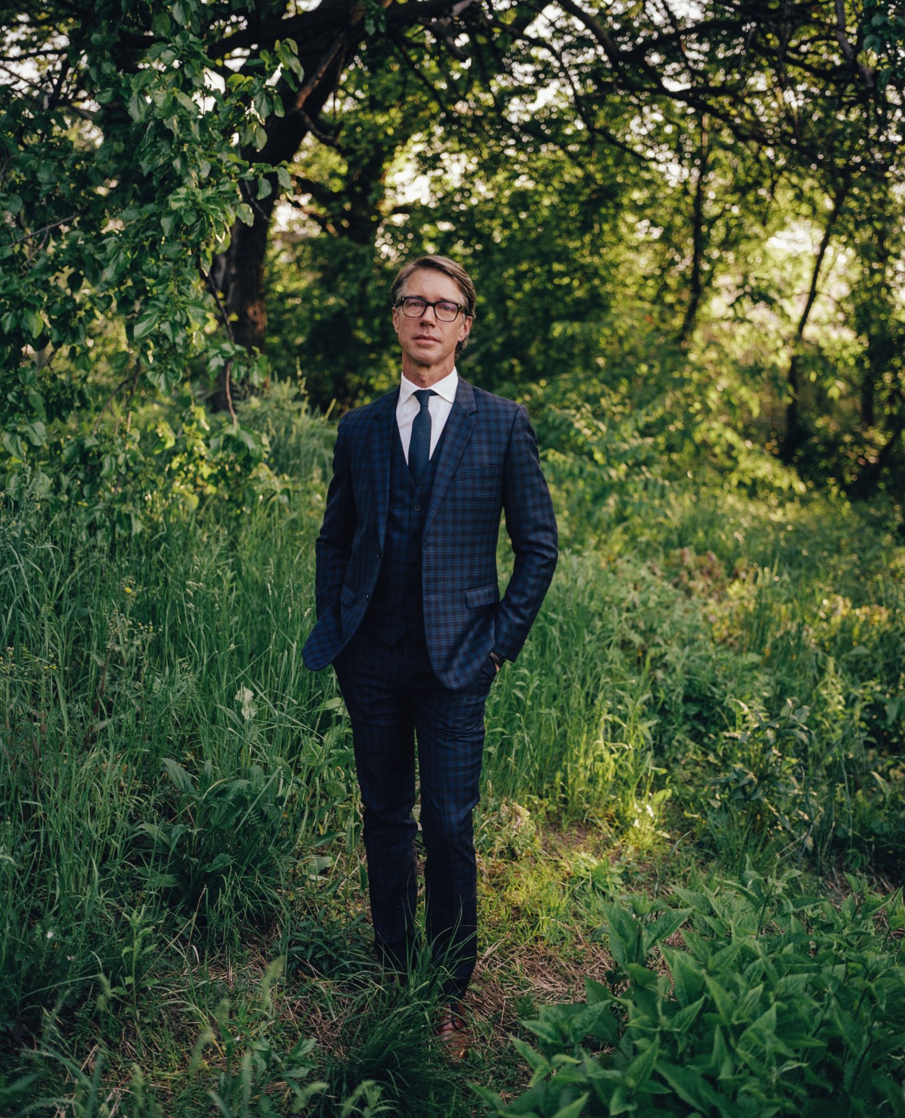 Thomas Woltz, CEO of Nelson Byrd Woltz, standing in a blue suit among tall grasses and trees at Brooklyn Naval Cemetery Park.