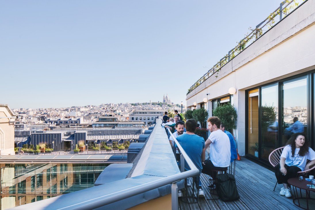 People having a meeting on a rooftop terrace at WeWork Paris with views of Sacré-Cœur basilica in the distance.