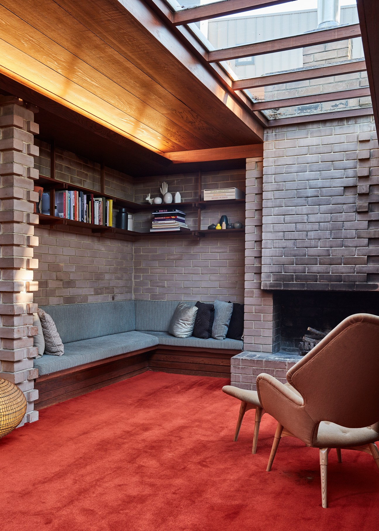 Modernist sitting room with brick walls, built-in seating, fireplace, skylight, red rug and mid-century furniture.