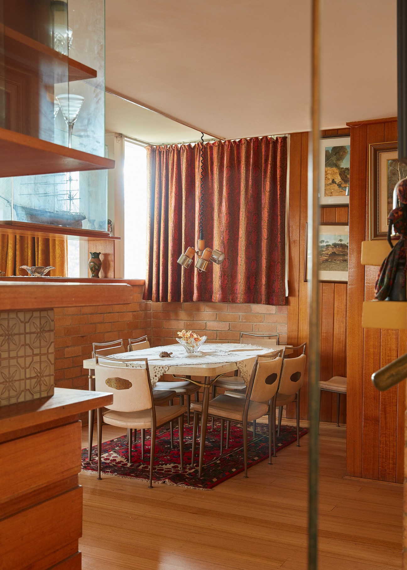 Mid-century modern dining area with wooden furniture, red curtains, and integrated kitchen in Muckle Flugga home.