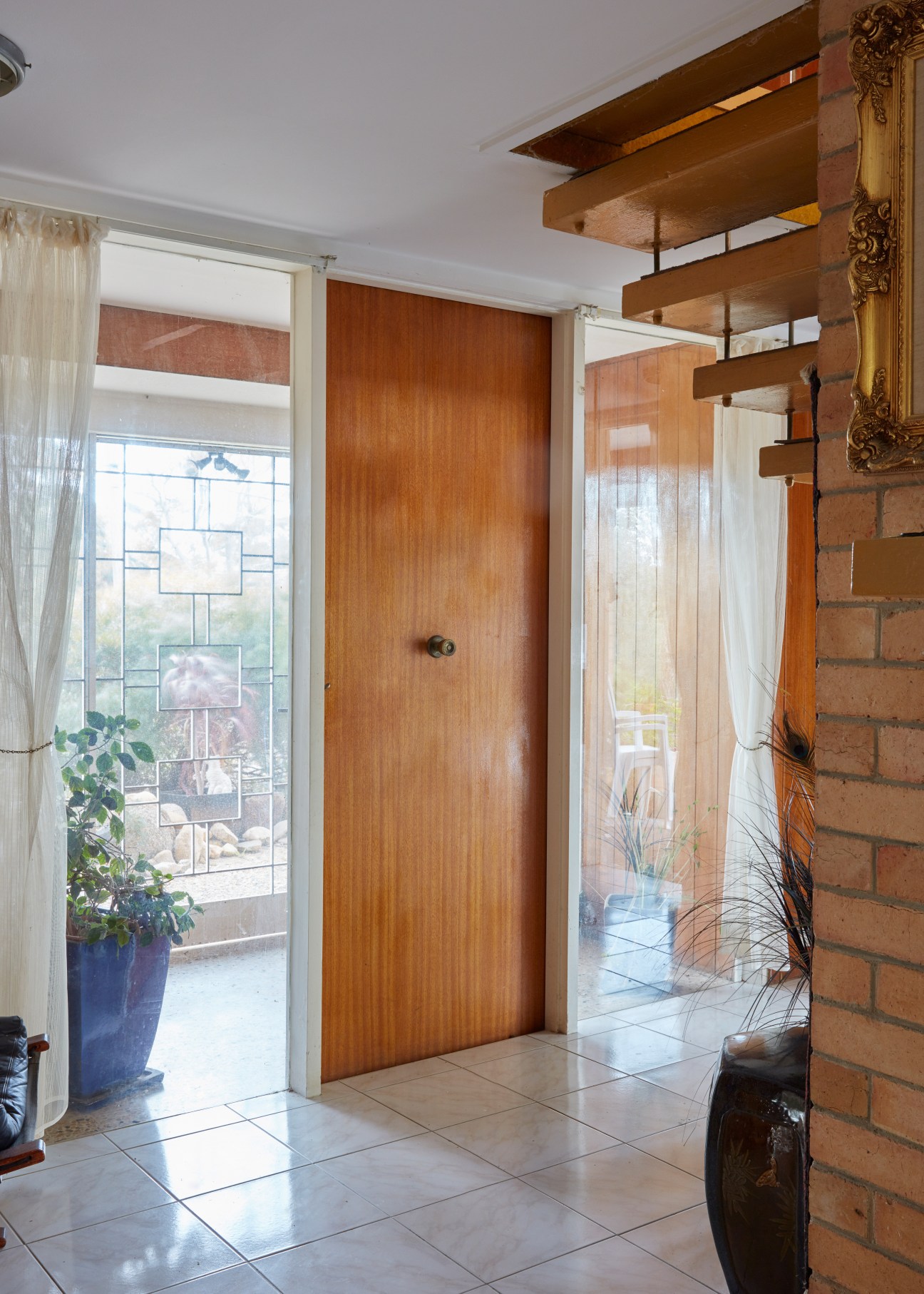 Wooden door entrance with brick wall, floating wooden shelves, and large window with geometric patterned glass.