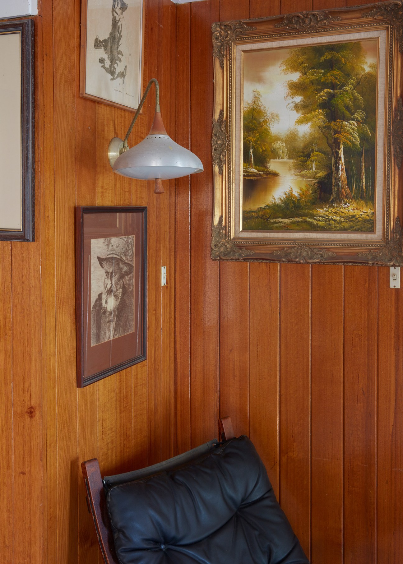 Wood-panelled interior wall with framed artworks, pendant lamp, and black leather chair.