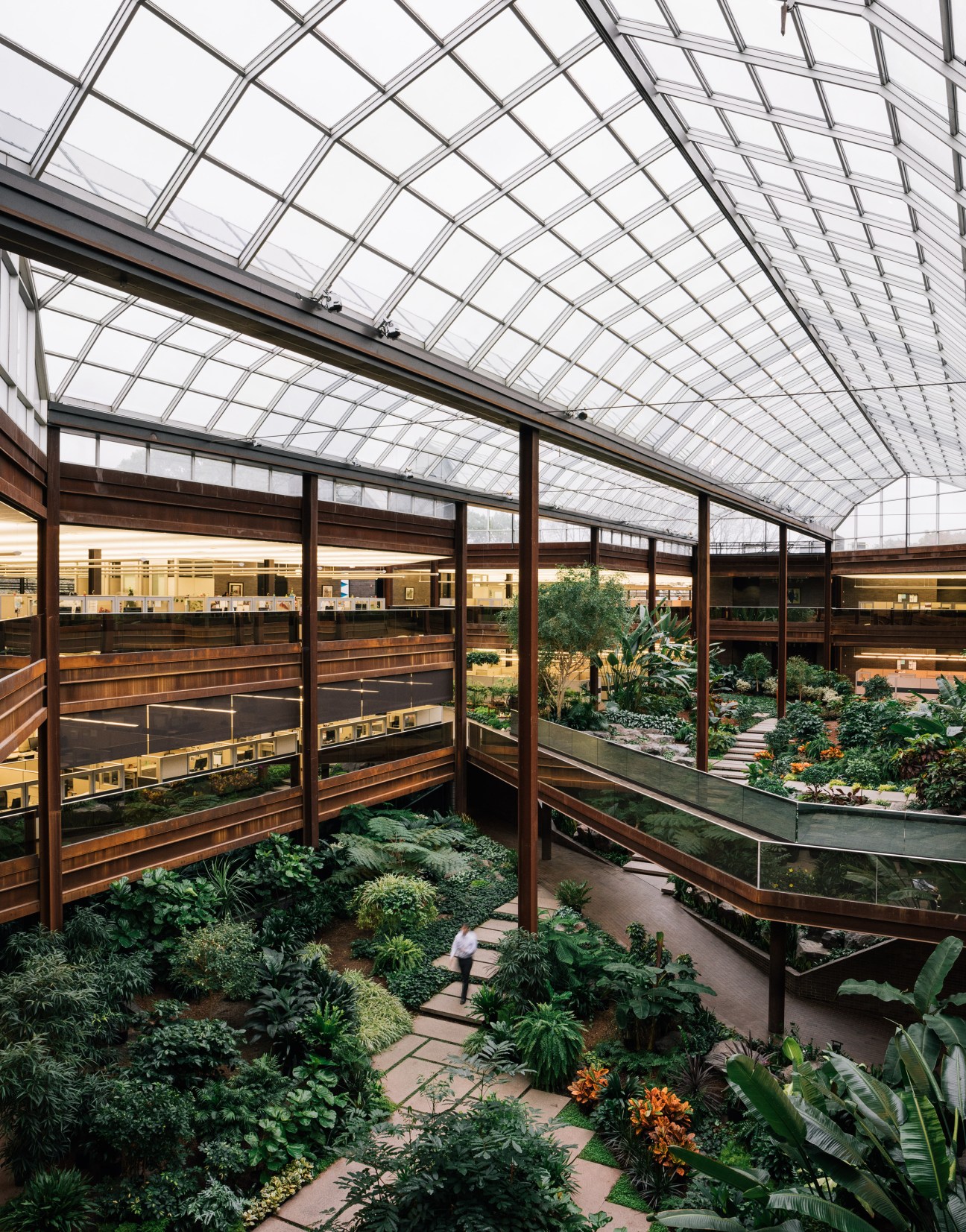 Glass atrium with steel framework and abundant greenery under a geometric skylight at John Deere headquarters.
