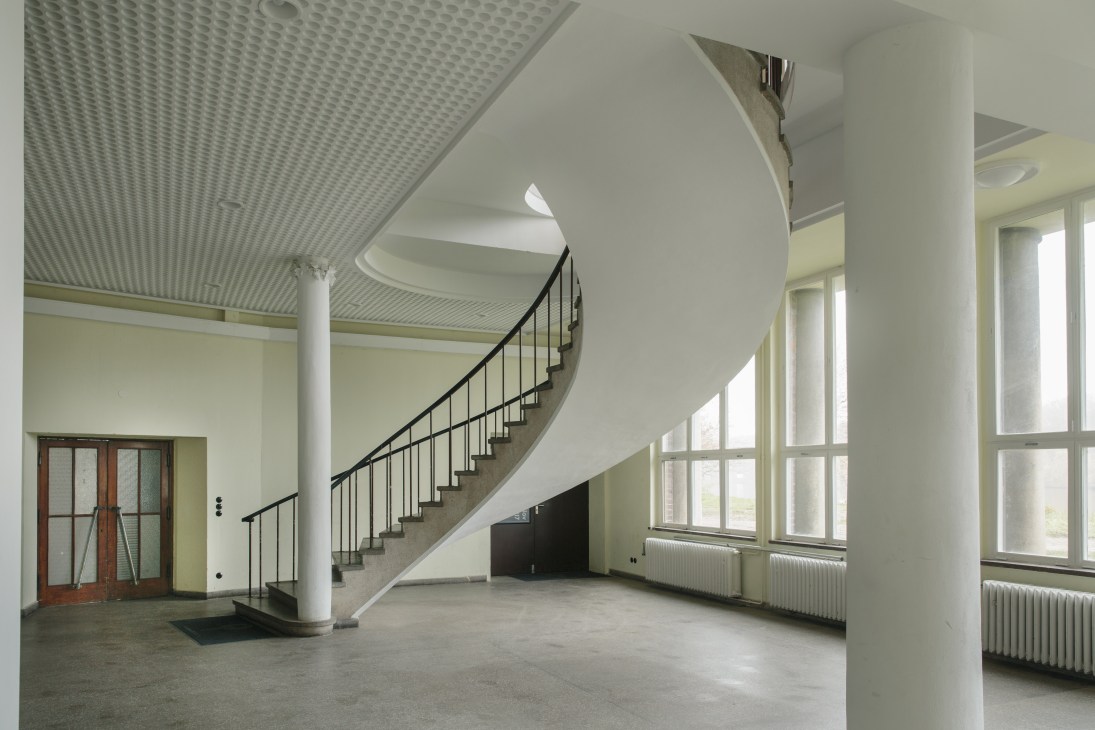 Modernist spiral staircase with black metal railings in a bright, minimal interior space at Funkhaus Block B