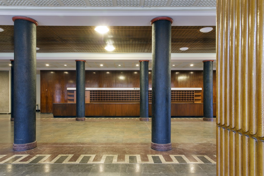 The expansive entrance hall of Funkhaus with blue cylindrical columns, wooden paneling, and geometric floor patterns.