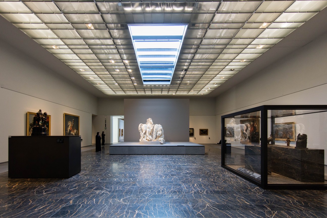 Gallery interior of the Louvre Abu Dhabi featuring a white marble sculpture on a central platform beneath a geometric latticed skylight designed by Jean Nouvel.