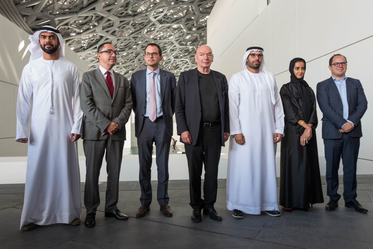 Seven team members standing in the Louvre Abu Dhabi atrium under the latticed dome roof designed by Jean Nouvel.