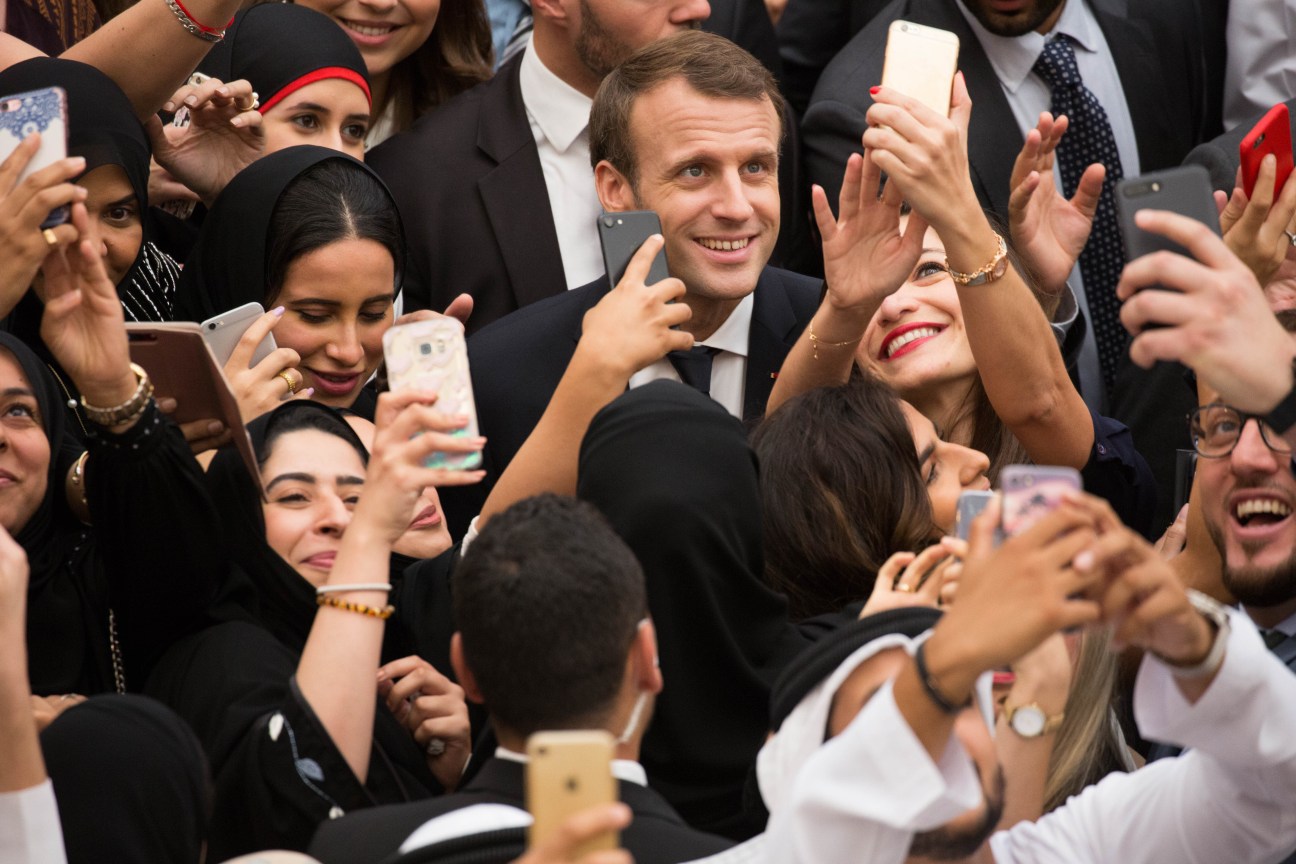 President Macron surrounded by a crowd of people holding smartphones at the Louvre Abu Dhabi opening.