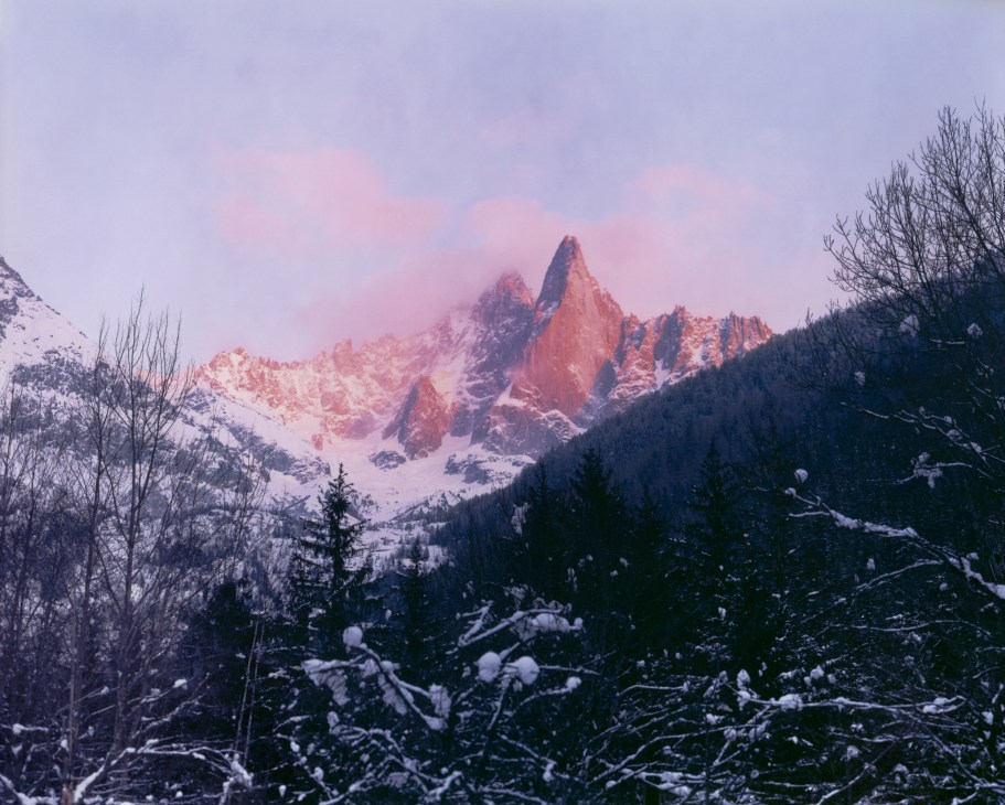 Pink alpenglow illuminates jagged granite peaks of Les Drus with forested slopes below in winter.