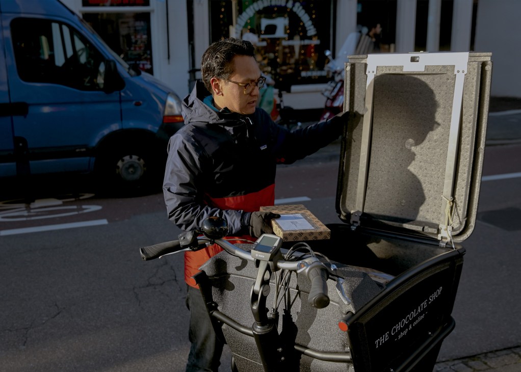 Man loading a package into an Urban Arrow cargo bike's storage compartment on a city street.