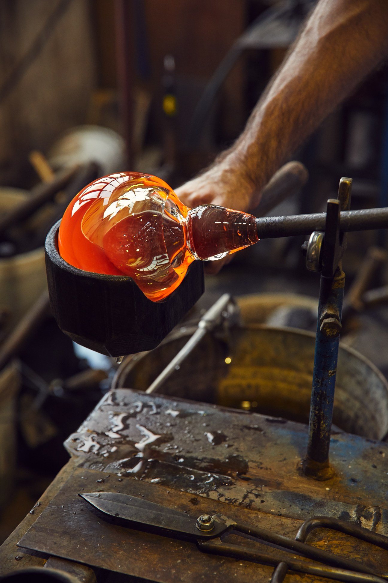 Molten orange glass on a blowpipe being shaped at Brokis glassworks factory.