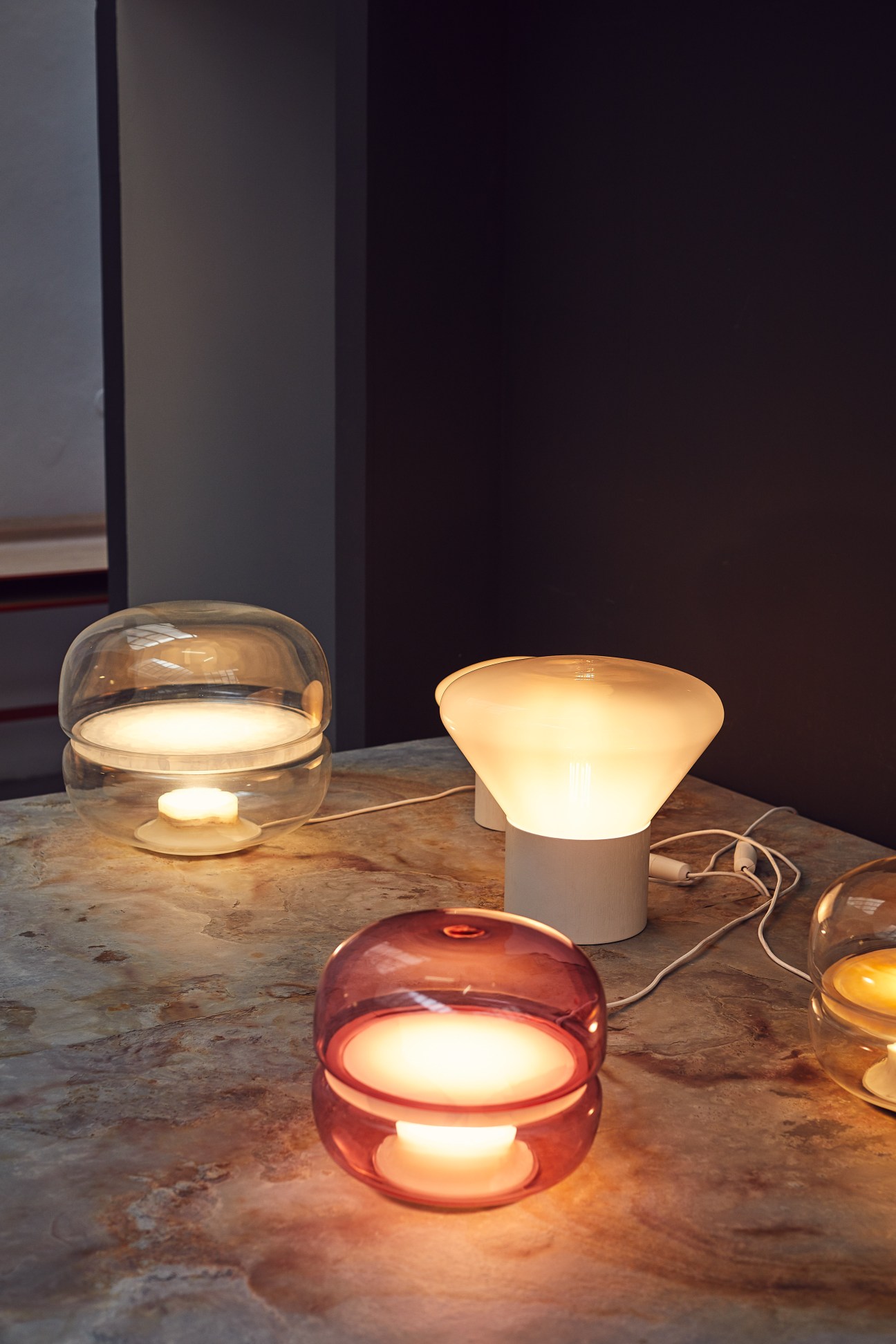 A selection of illuminated glass lamps by Brokis featuring various designs in clear, white, and red tones.