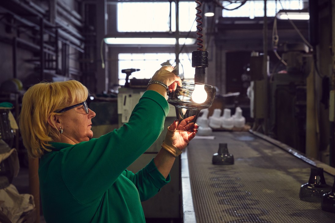 A worker in green inspects a mouth-blown glass lighting fixture at Brokis factory in Czech Republic.
