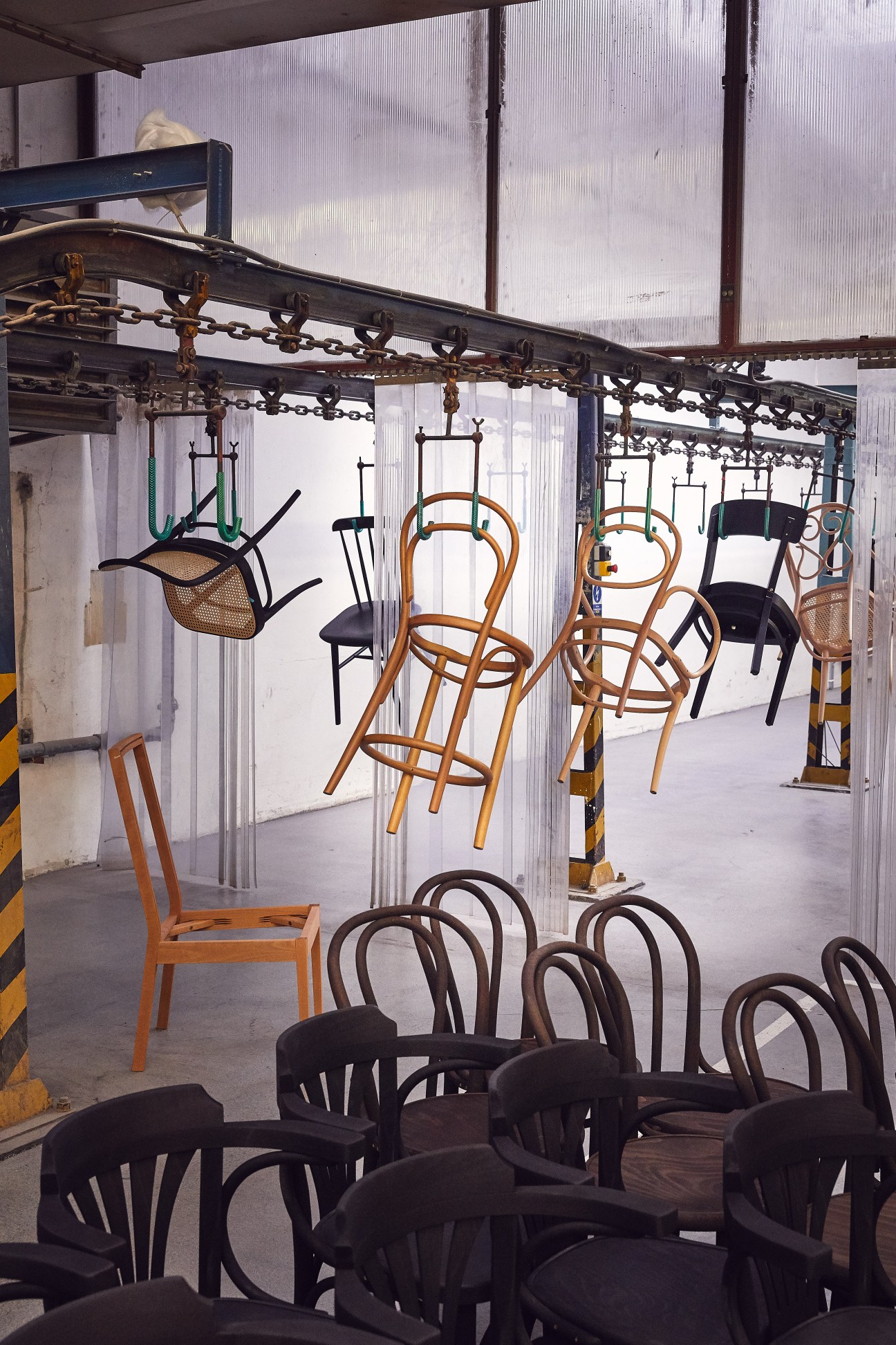 Wooden chairs suspended from an overhead conveyor system at Ton furniture factory production line.