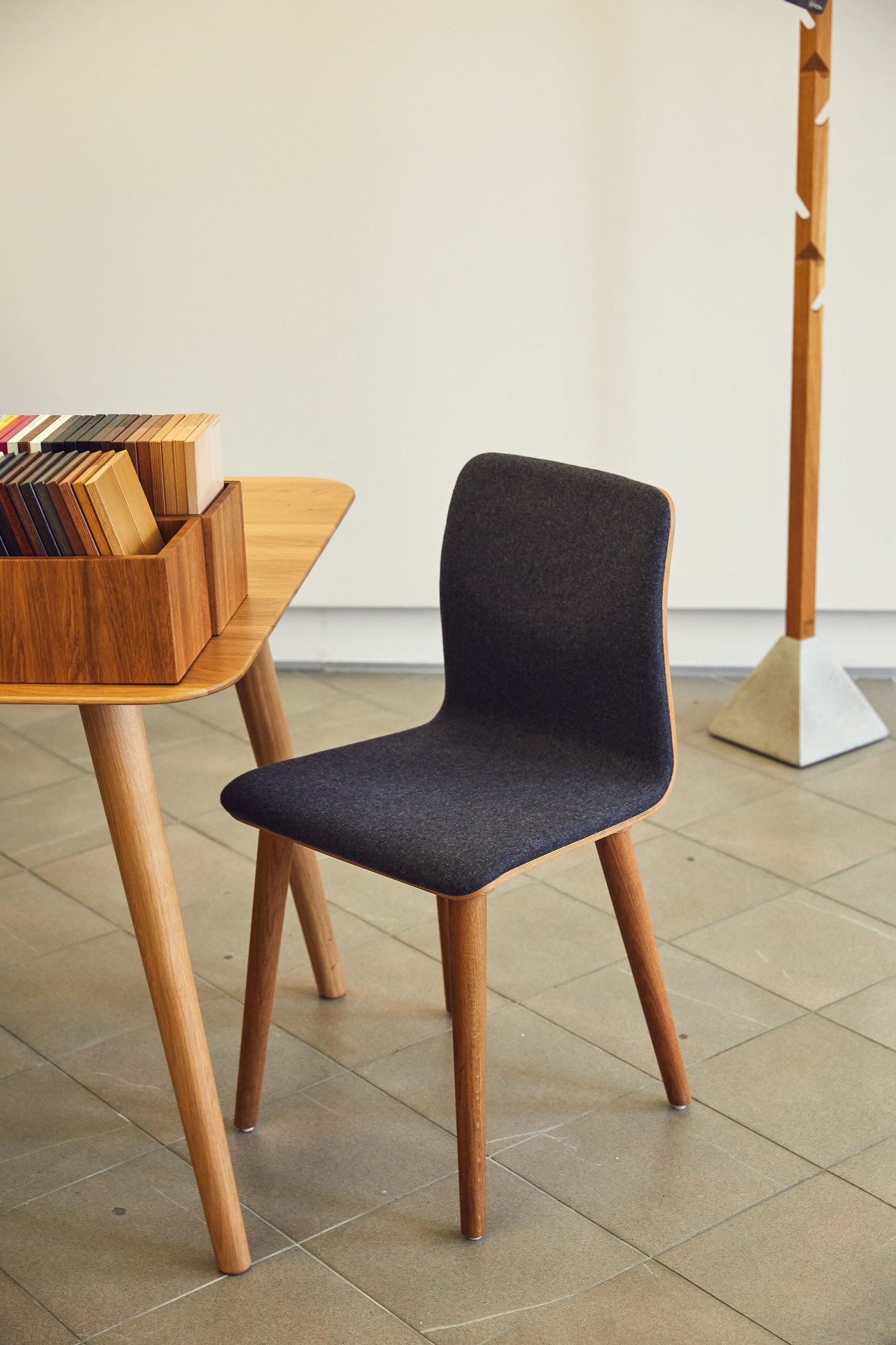 Modern wooden chair with black upholstered seat next to a wooden desk with shelving in a minimalist showroom.